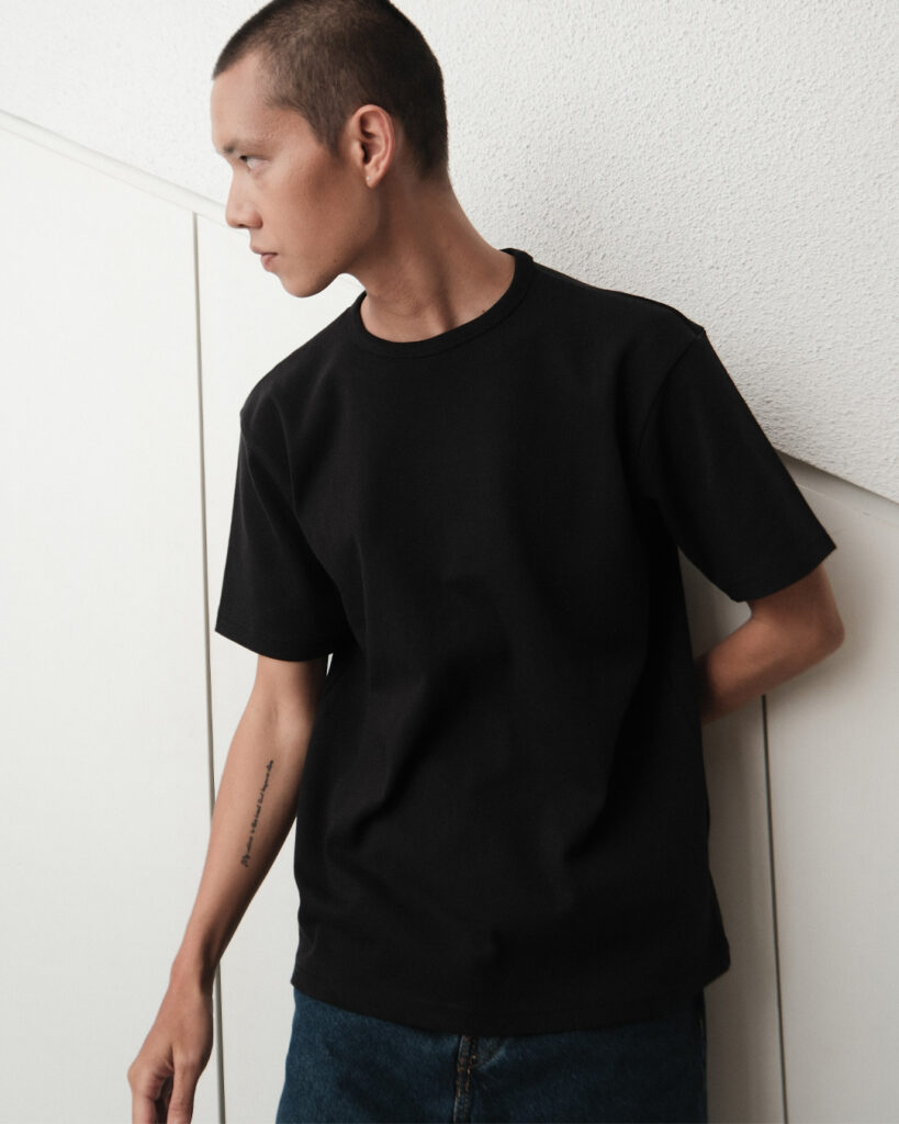 Man in the black Regular T-shirt leaning against a wall